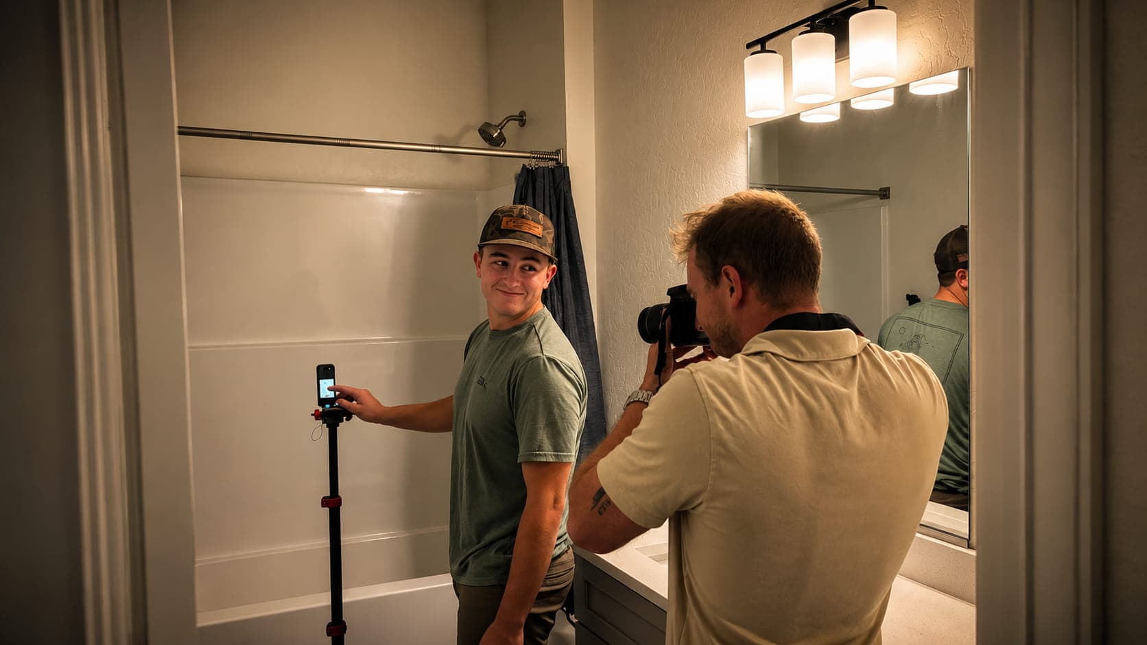 Photographer captures a man in a cap posing by a bathtub with a phone tripod.